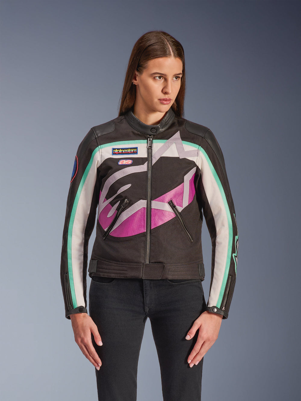 Alpinestars Idles Women's Jacket, Motorcycle Jacket, Black with Off White Purple and Teal Color Block Design, Vintage Racing-Inspired Style with Large Abstract Logo on Chest, Branded Patches and Front Zipper, Worn by Model with Black Jeans