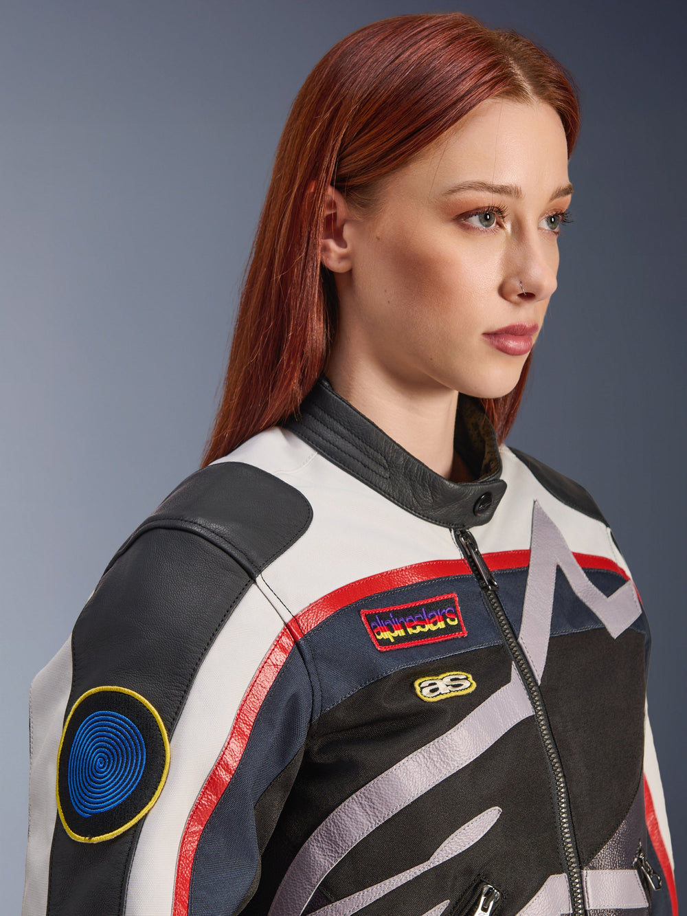Alpinestars Idles Women’s Jacket, Off White, Flame Red and Black, featuring vintage-inspired racing patches and a wrap-around logo, textile and leather construction, urban motorcycle style worn by a model.