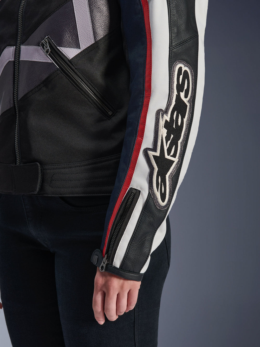 Alpinestars Idles Women's Jacket, urban motorcycle jacket, Off White Flame Red Black, close-up of the sleeve with a large embroidered Alpinestars logo, red and white racing stripes, black textile and leather construction, and metal zipper accents.