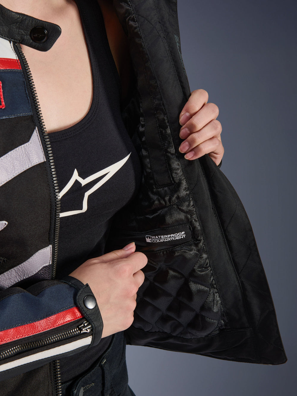 Alpinestars Idles Women’s Jacket, interior detail showing black quilted lining and labeled waterproof compartment, worn over a black logo tank top, functional motorcycle riding gear for women