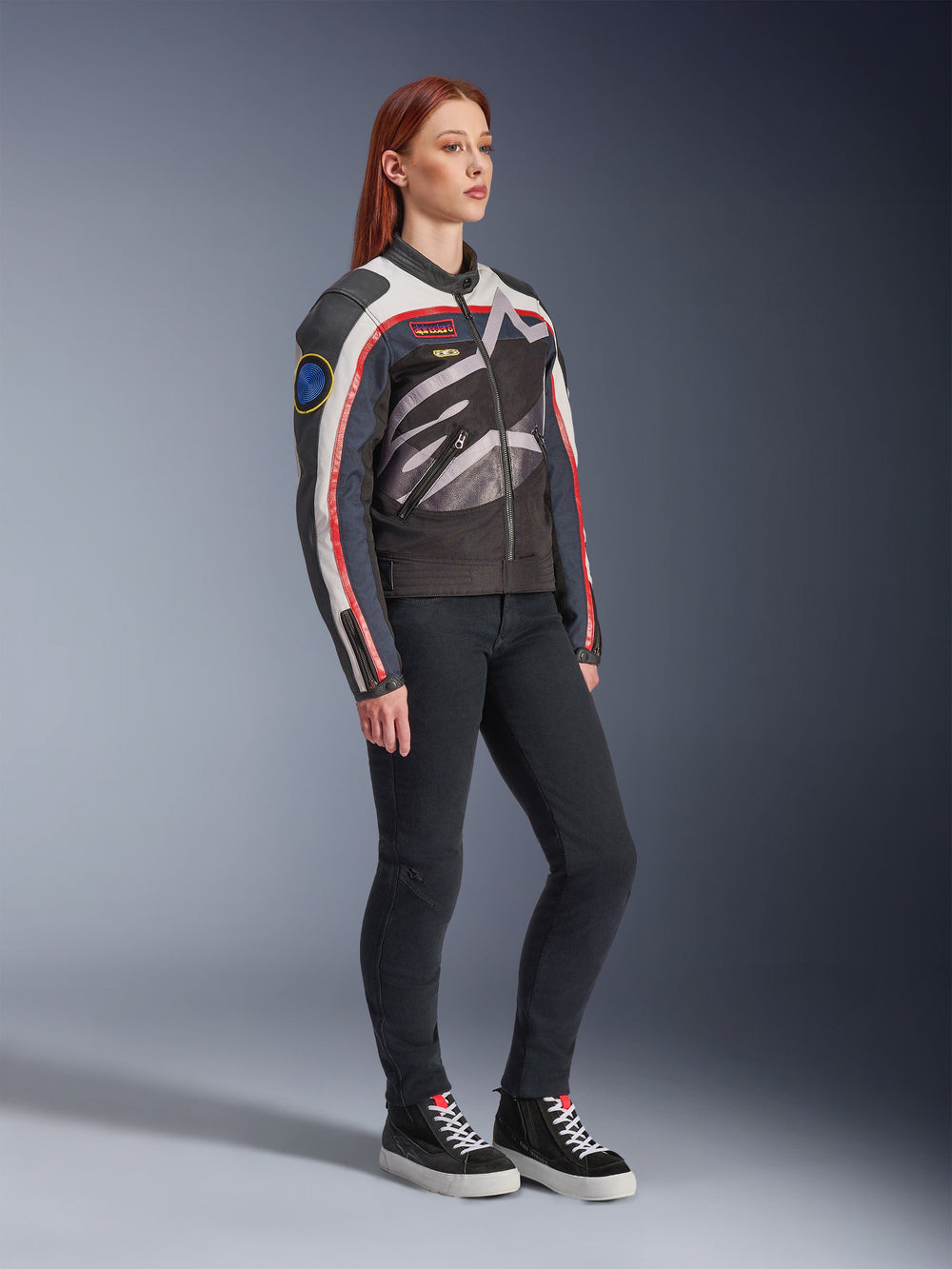 Alpinestars Idles Women's Jacket, Motorcycle Jacket, Off White Flame Red and Black, featuring a large wrap-around Alpinestars logo and vintage racing-inspired patches, worn with black pants and high-top sneakers, contemporary urban riding gear