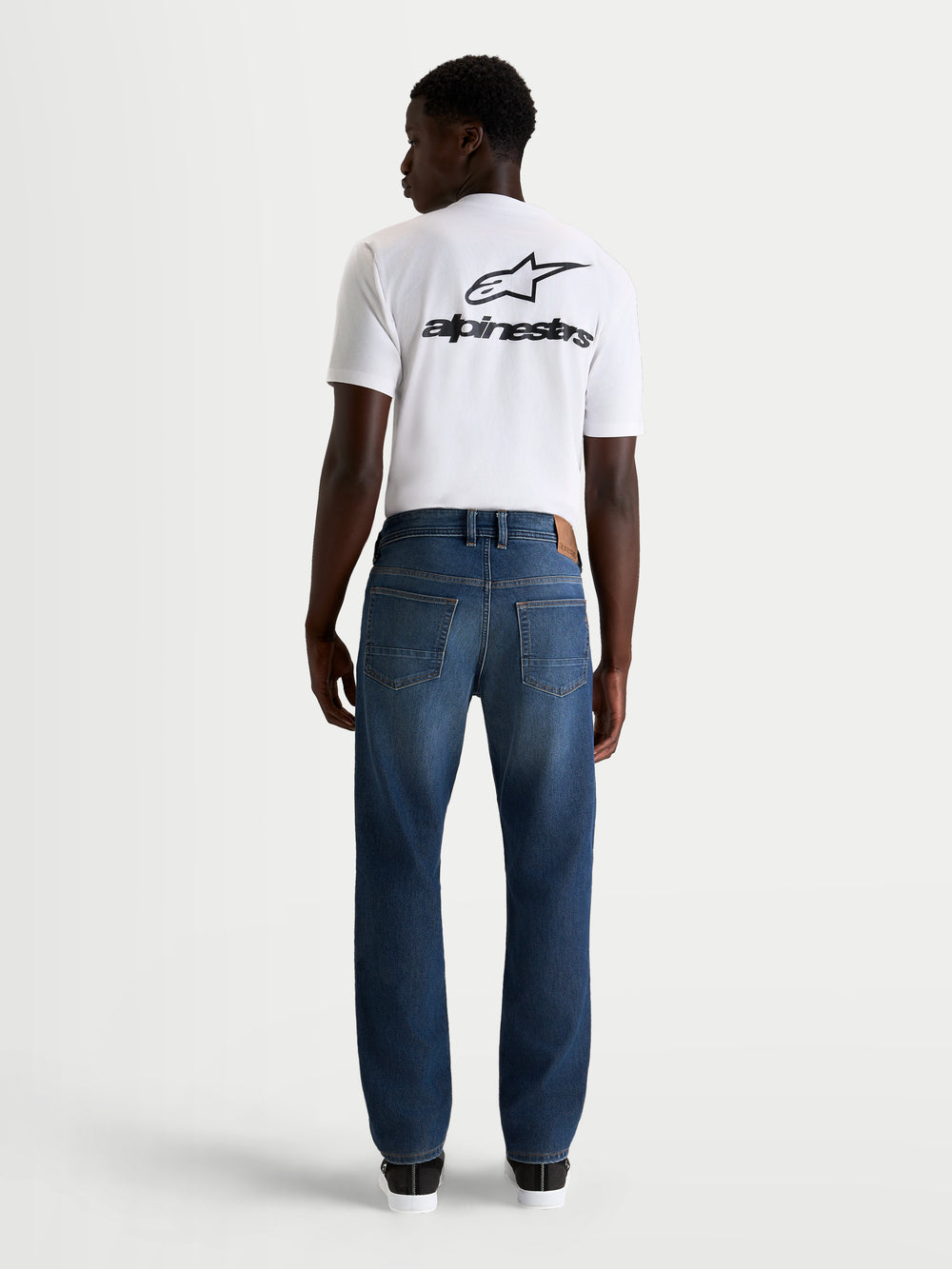 Alpinestars Flex-AST 8 Denim Pants Short, men's urban motorcycle riding jeans in medium blue, rear profile view on a model wearing a white t-shirt, AA-certified protective single-layer denim with stretch comfort.