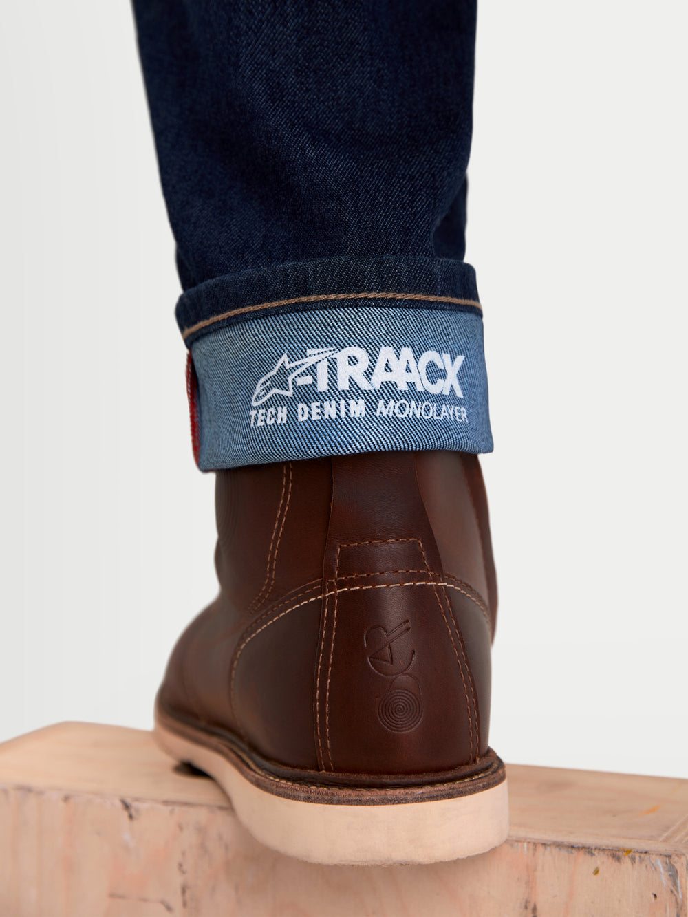Alpinestars Flex-AST 7 Denim Pants Short, urban motorcycle riding jeans in dark blue, close-up view of the cuffed hem showing A-TRAACX tech denim monolayer branding and brown leather boots