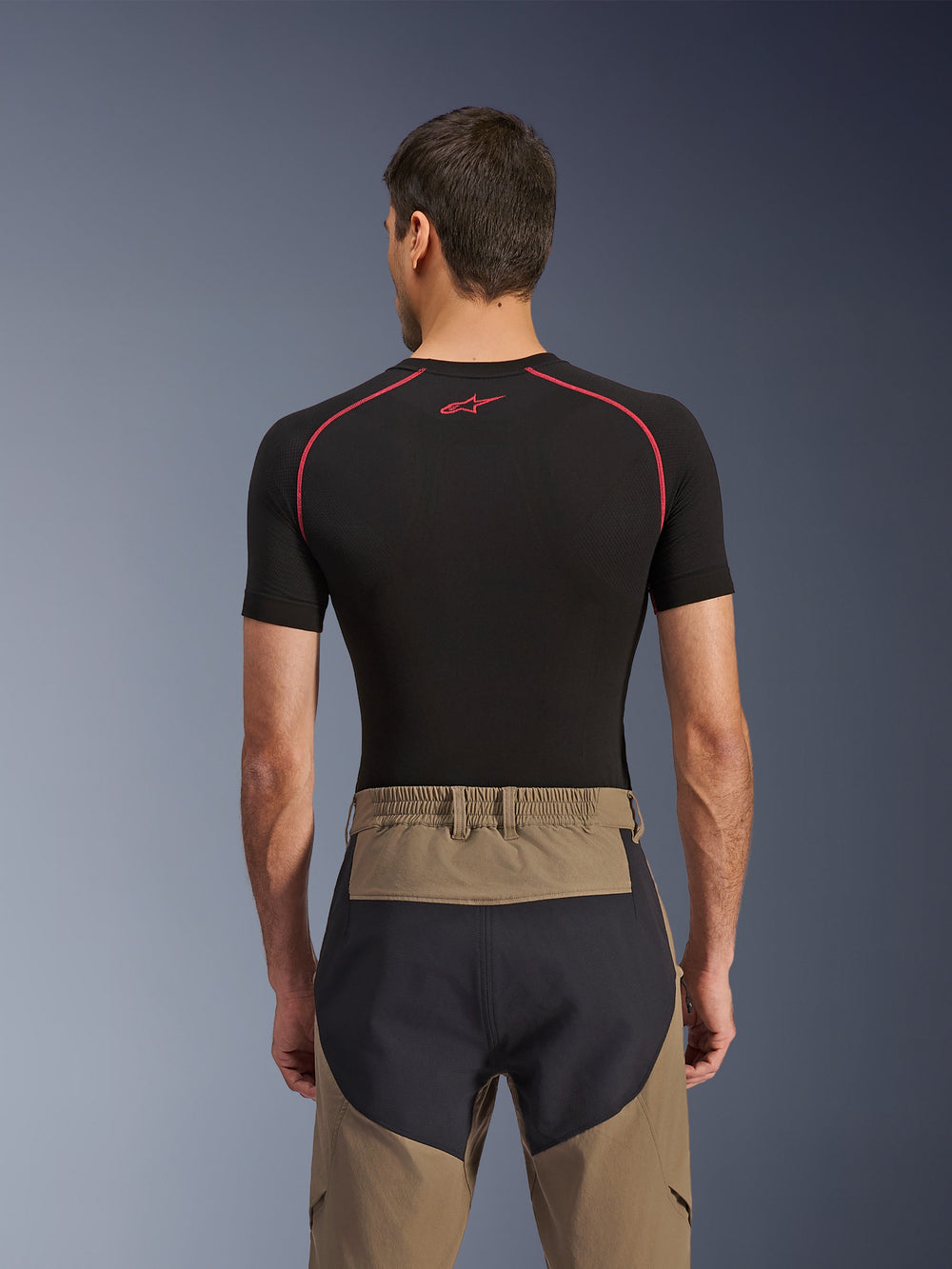 Alpinestars Flex-AST Explorer Pants, rear view on model, Walnut Black, featuring tan textile with reinforced black seat panels and an elasticated waistband, paired with a black short-sleeve base layer with red stitching.