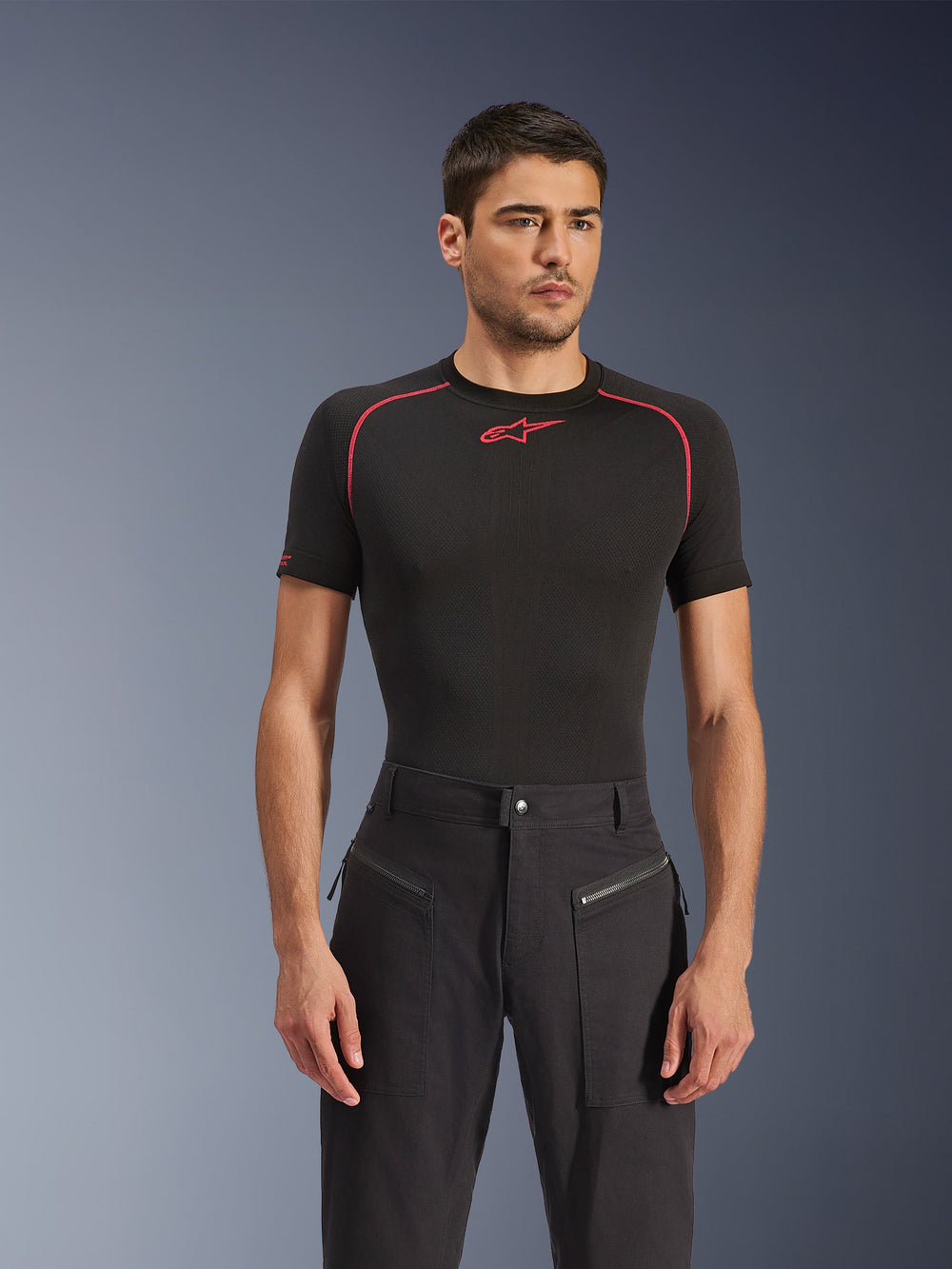 Male model wearing Alpinestars Flex-AST Canvas Pants in Black, urban motorcycle pants featuring visible zippered front pockets and a workwear-inspired design, paired with a black base layer with red accents.