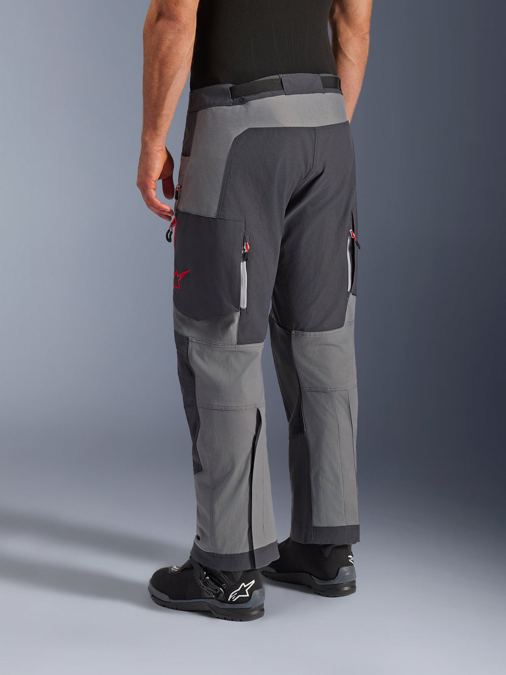 Alpinestars Maxdura Dual Pants, Adventure Motorcycle Pants, Dark Gray and Deep Gray, rear view featuring multi-panel construction with red zipper accents and star logo, paired with black Alpinestars boots, designed for dual-sport performance