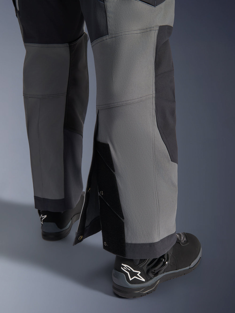Alpinestars Maxdura Dual Pants, Adventure Motorcycle Pants, Dark Gray and Deep Gray, close-up view of adjustable over-the-boot leg hem with snap closures and reinforced panels, worn with black Alpinestars boots, rugged technical design for dual-sport riding