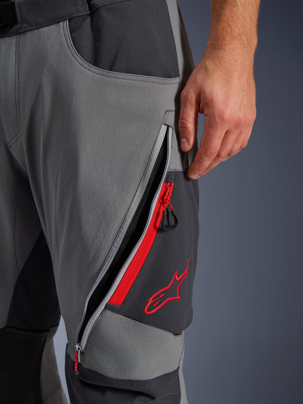 Alpinestars Maxdura Dual Pants, Dark Gray and Deep Gray adventure motorcycle pants, close-up view of open zippered thigh vent with red highlights and embroidered red star logo, technical stretch fabric design