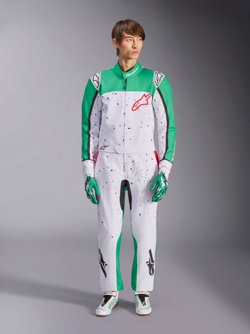 Alpinestars KMX-9 V3 Graphic 6 Suit, White Green and Red, one-piece karting suit featuring a black splatter graphic pattern, green panels on sleeves and legs, red Alpinestars chest logo, worn with matching racing gloves and shoes