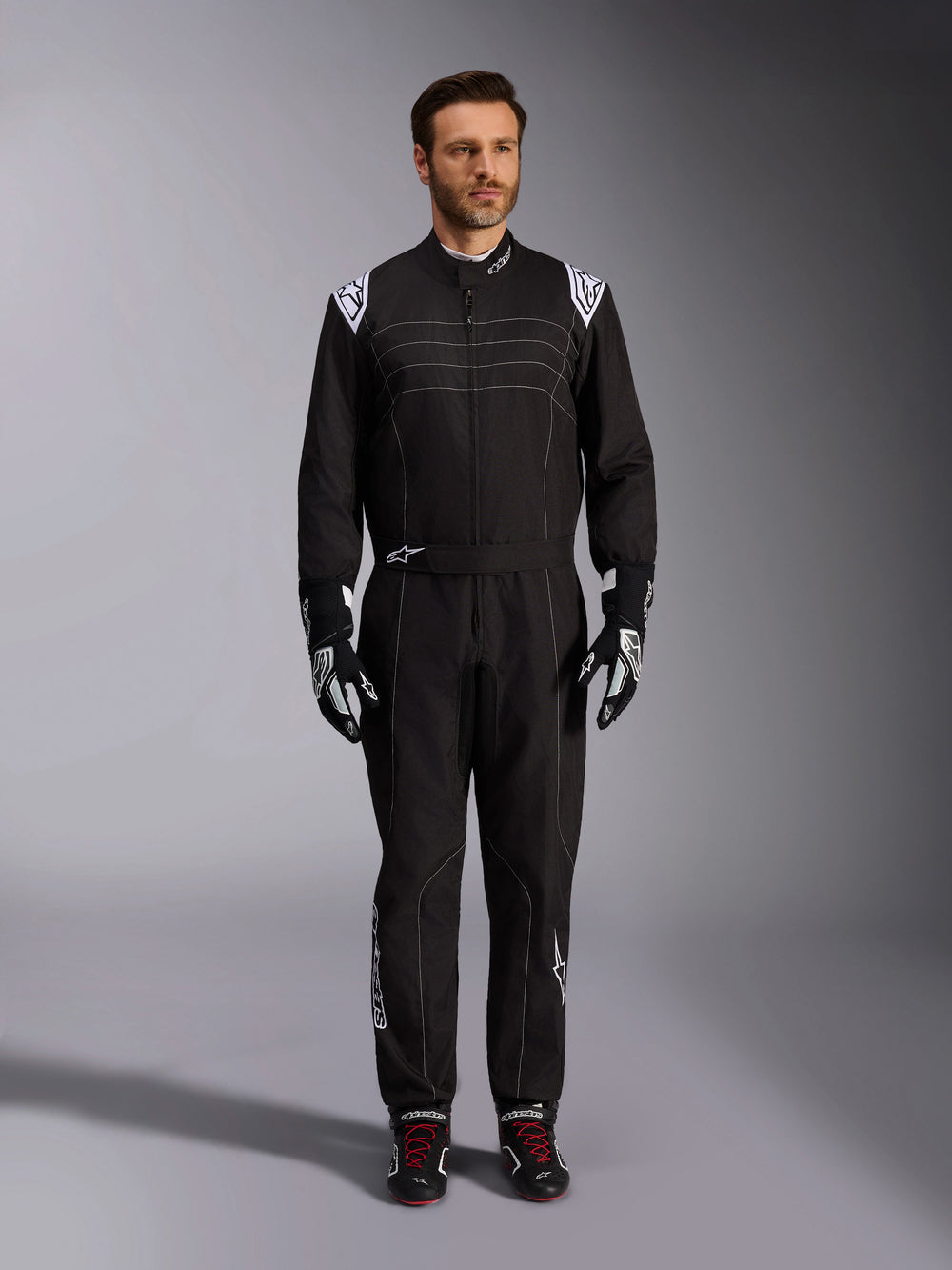 Alpinestars KMX-9 V3 Suit, Black and White Karting Suit, full-length view on a model, featuring white shoulder logos and accents, styled with black and white racing gloves and black shoes with red laces, athletic-regular fit for professional karting gear.