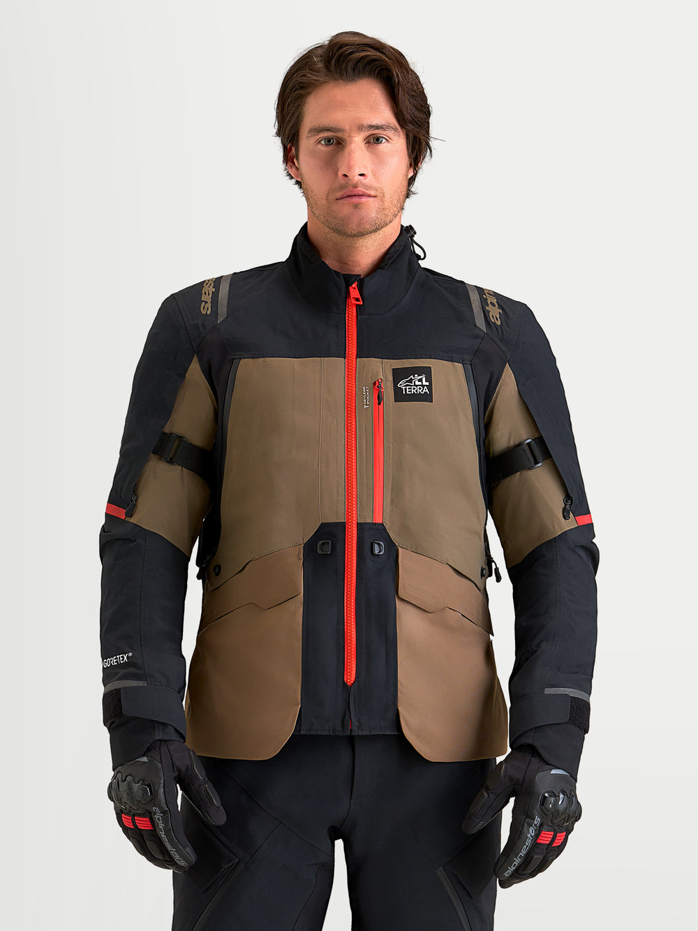 Alpinestars St-7 V2 2L Gore-Tex Jacket, men's adventure touring motorcycle jacket in walnut and black, featuring a waterproof GORE-TEX shell, bright red central zipper, and CE Level 2 armor, worn by a male model