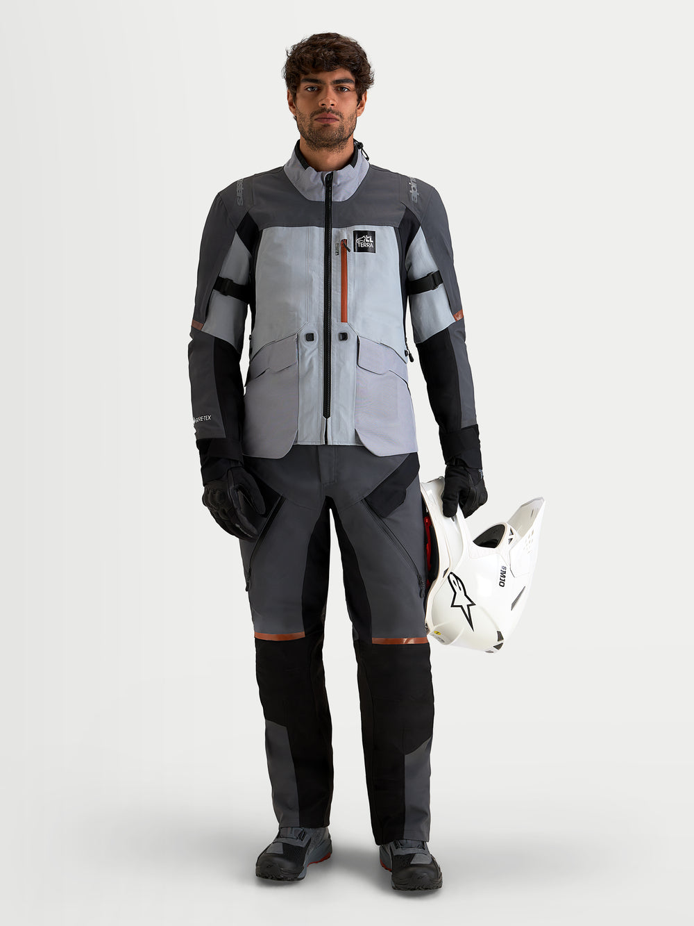 Alpinestars St-7 V2 2L Gore-Tex Jacket, Men's Adventure Touring Motorcycle Jacket in Mid Gray and Black, waterproof textile construction with CE-certified protection, worn by a model holding a white helmet
