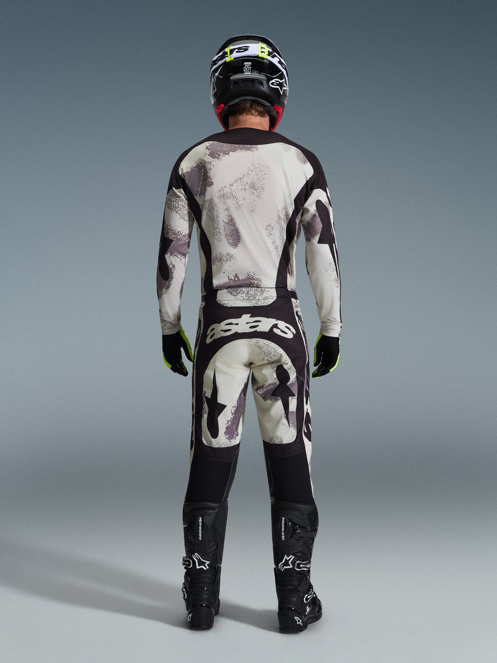 Motocross rider from behind wearing the Alpinestars 2026 Racer Lahnd Pants in Sand Camo, matching long-sleeve jersey with gray camouflage pattern, black motocross boots, black helmet, and 