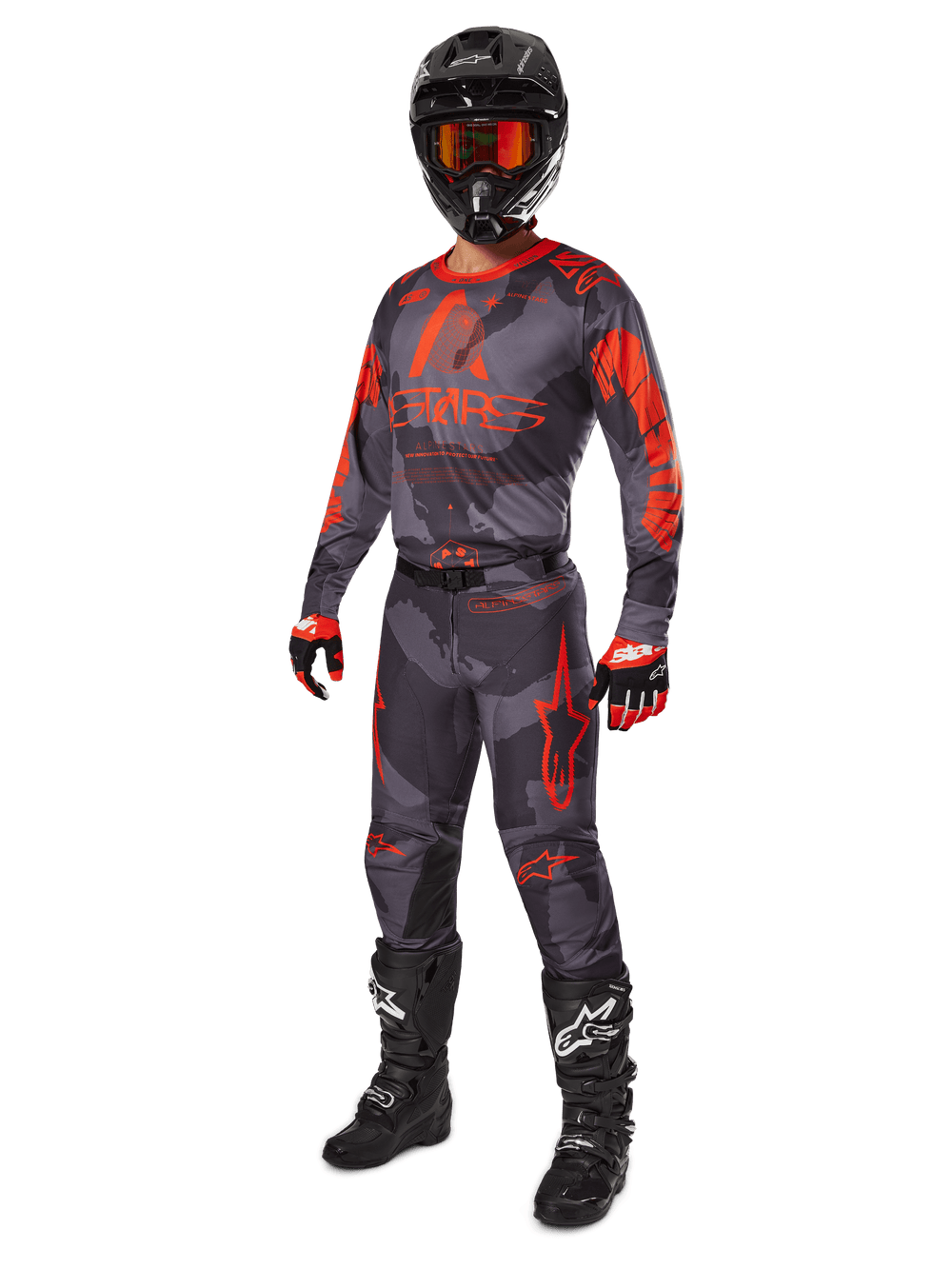 Motocross rider wearing the Alpinestars 2025 Racer Hollow gear set, Gray Camo and Orange Fluo pants and jersey, black helmet with orange goggles, black and red gloves, and black boots, coordinated professional racing outfit for off-road performance