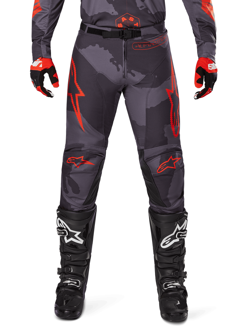 Alpinestars 2025 Racer Hollow Pants, Motocross Pants, Gray Camo and Orange Fluo, worn with black and white motocross boots and matching gear, featuring bold orange logos on thighs and knees, durable camouflage design for off-road racing