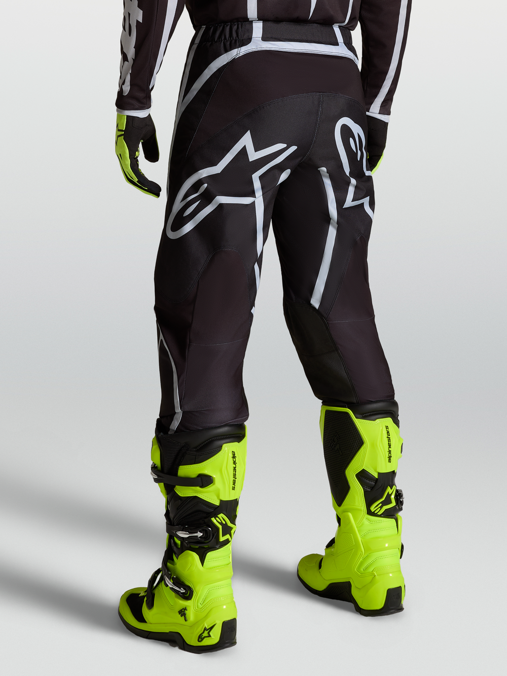 Alpinestars Fluid Apex V2 Pants, Black and Silver motocross pants for men shown on a rider with fluorescent yellow boots.