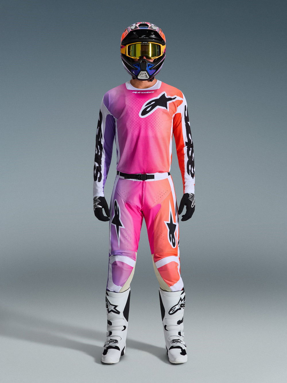 Motocross rider wearing the 2026 Racer Air Portl Jersey and matching pants, featuring a pink, purple, and orange gradient with black Alpinestars logos, white racing boots, black gloves, and a multicolor helmet, professional off-road racing gear.