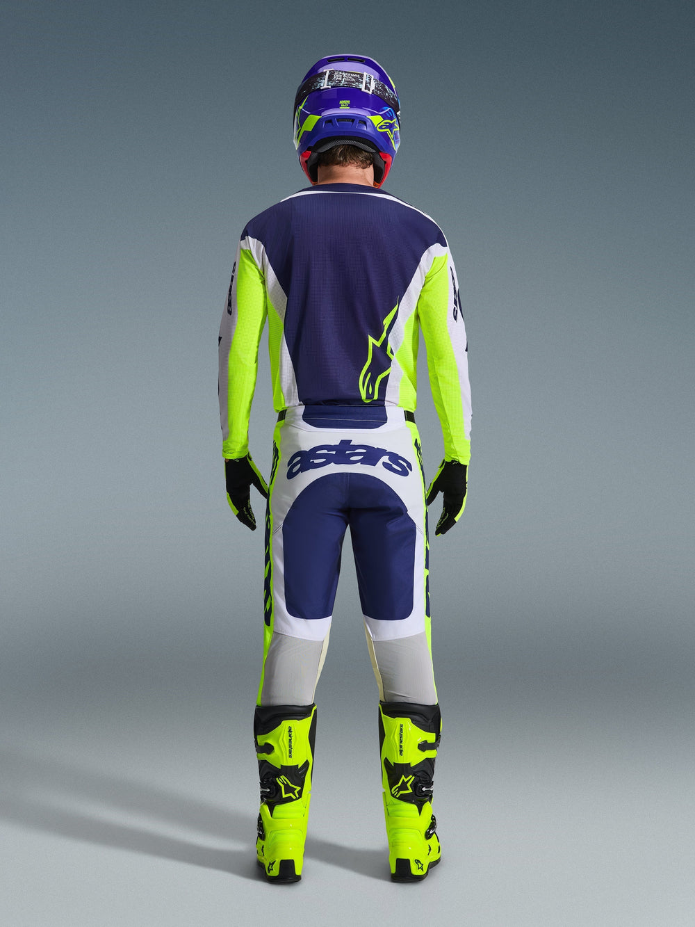 Back view of a motocross rider wearing the Alpinestars 2026 Racer Air Riway Jersey and matching pants in Light Gray Yellow Fluo Blue, paired with bright yellow fluo boots and a coordinated helmet, showing a complete off-road racing gear set.