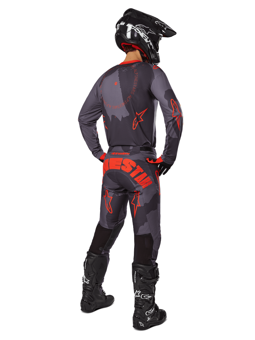 Motocross rider from a rear view wearing the Alpinestars 2025 Racer Hollow Jersey in Gray Camo Orange Fluo, matching camo pants with orange Alpinestars text, black helmet, and black boots, coordinated gear set for off-road riding