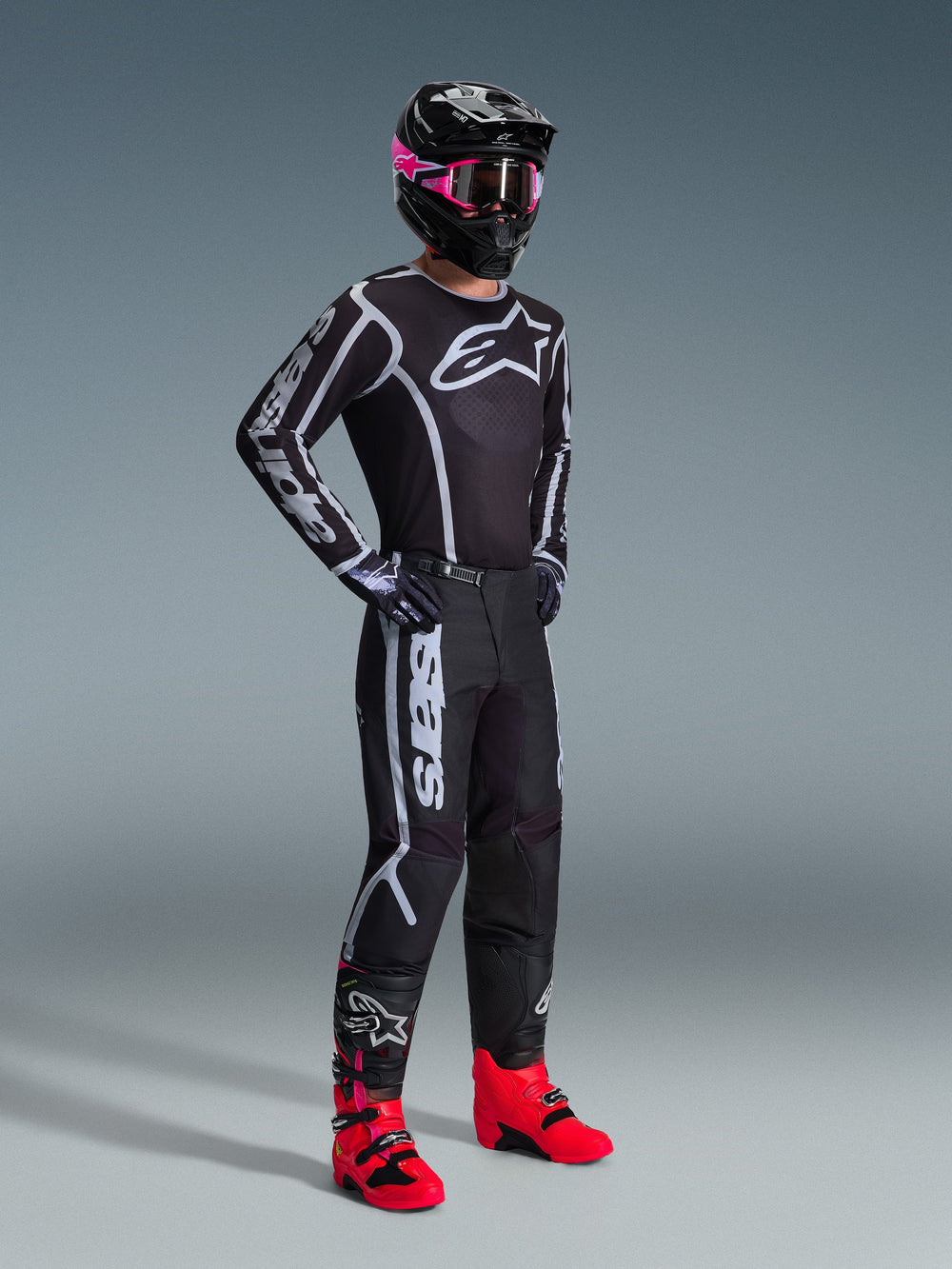 Motocross rider wearing 2026 Fluid Apex Jersey, Black and Gray, paired with matching pants, black helmet with pink goggles, and bright red boots, featuring bold white Alpinestars branding on the chest and sleeves, coordinated professional off-road racing outfit.