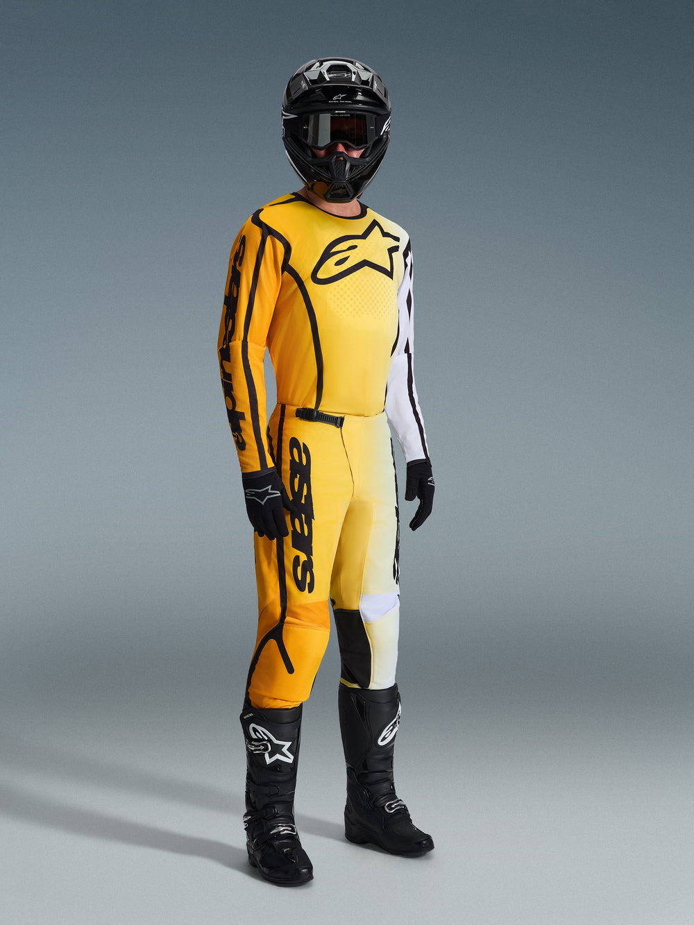Motocross rider wearing the Alpinestars 2026 Fluid Apex Jersey in Yellow and Black, featuring a yellow to white gradient design with a large black chest logo, paired with matching pants, black helmet, and black boots, complete racing gear for off-road motocross.