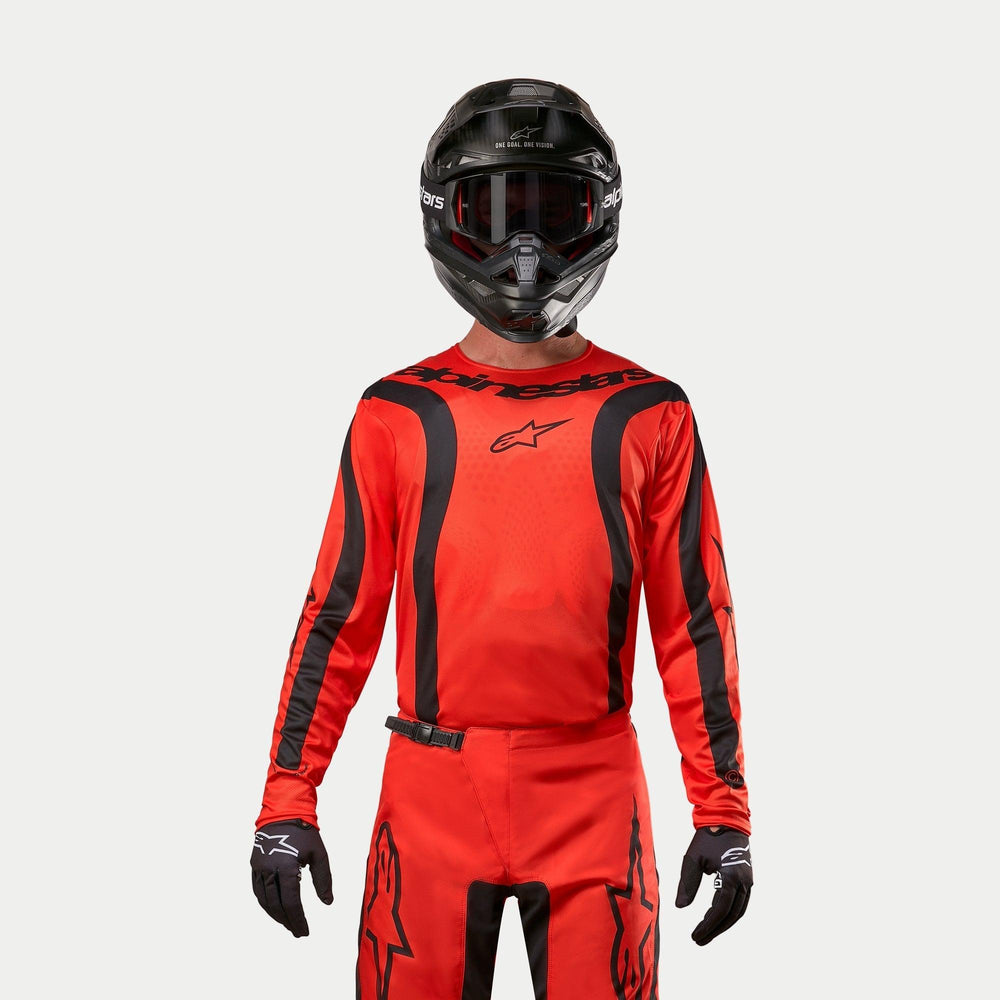 Motocross rider wearing Alpinestars 2024 Fluid Lurv Jersey, Hot Orange and Black, matching motocross pants, black helmet with goggles, and black gloves, coordinated gear for off-road racing