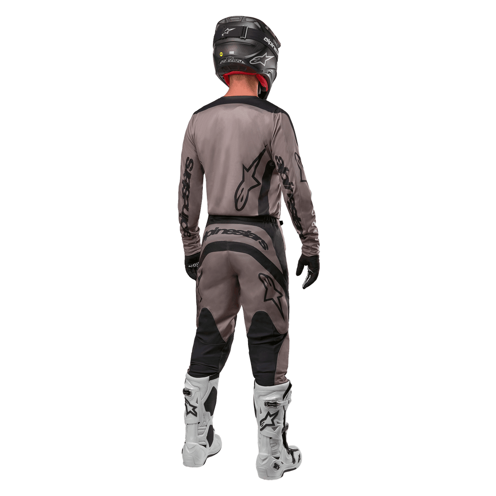 Alpinestars 2024 Fluid Lurv Jersey, Motocross Jersey, Mud Black, rear view of motocross rider wearing matching racing gear, black helmet, and white boots, featuring bold black Alpinestars logos and an athletic fit for off-road performance.