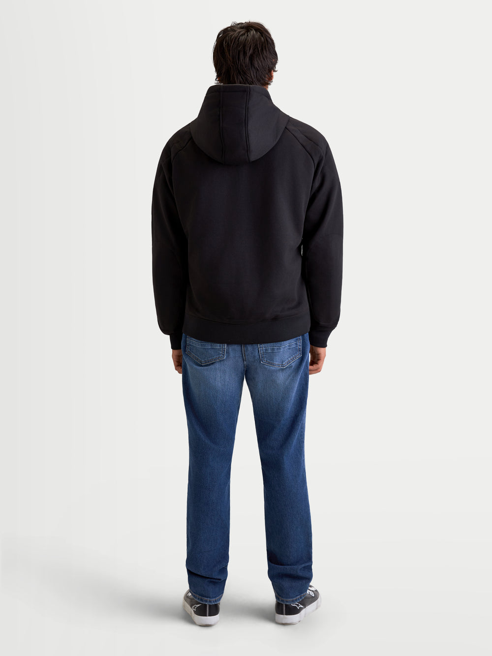 Alpinestars Ageless Hoodie, men's urban motorcycle hoodie in black, rear profile view on a model wearing jeans and casual riding shoes, featuring a fixed hood and protective textile construction.