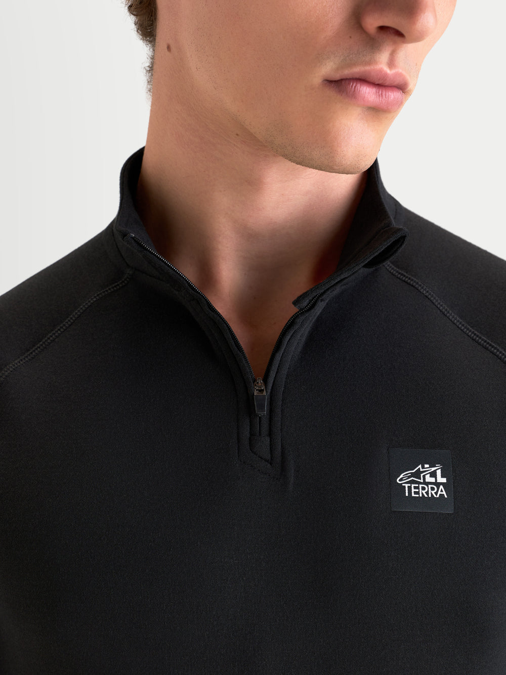 Alpinestars AT-8 Merino Top Layer, men's all-terrain adventure motorcycle tech layer in black, close-up view showing the technical collar, front zipper, and All Terra branding worn by a model.
