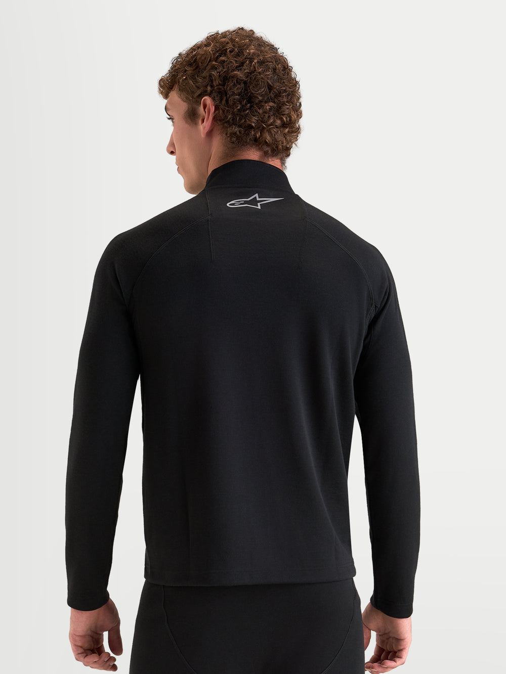 Alpinestars AT-8 Merino Top Layer, men's long sleeve motorcycle base layer in black, rear view showing a model wearing the thermal dual-layer merino wool top with a reflective Astar logo on the collar
