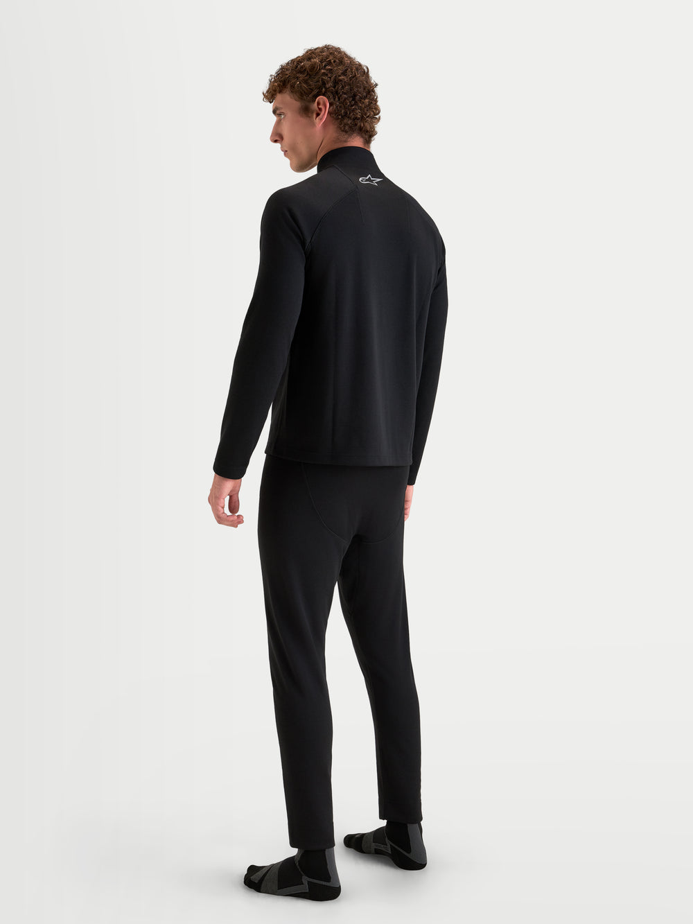 Alpinestars AT-8 Merino Top Layer and AT-8 Merino Bottom Tech Layer, men's adventure motorcycle base layers in black, rear view on a model showing dual-layer merino wool thermal construction and raglan sleeves