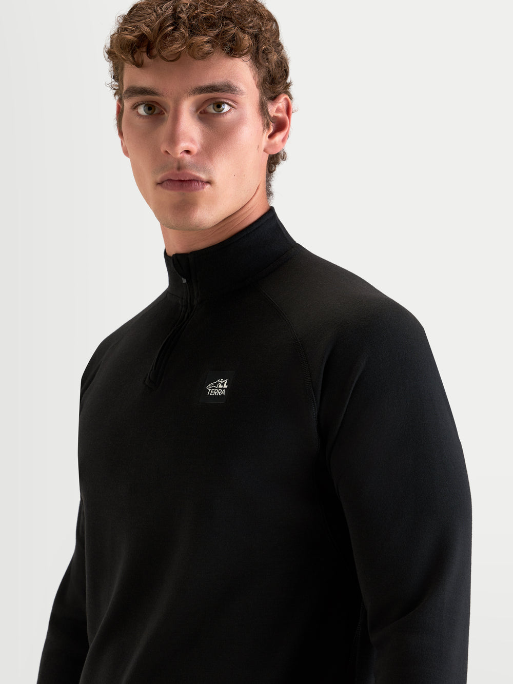 Alpinestars AT-8 Merino Top Layer, men's motorcycle thermal base layer in black, close-up view on a model showing the streamlined collar, raglan sleeves, and All Terra logo detail