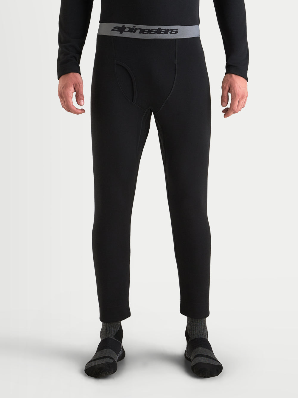 Alpinestars AT-8 Merino Bottom Tech Layer, men's motorcycle thermal base layer in black, featuring seamless Merino-blend construction, elasticated waistband with Alpinestars branding, and functional fly opening worn on a model.