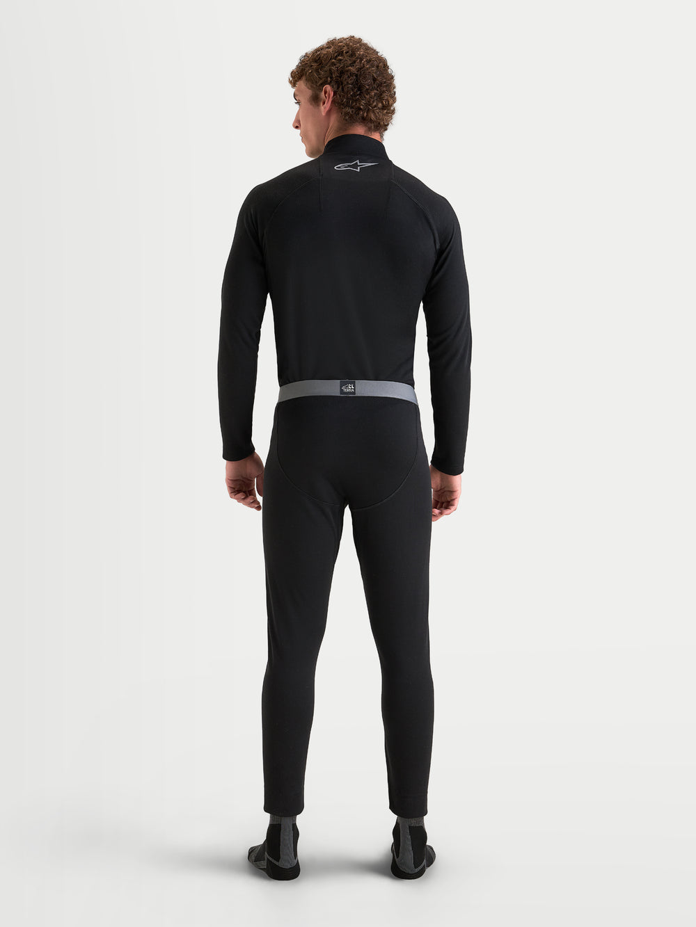Alpinestars AT-8 Merino Bottom Tech Layer, men's motorcycle base layer pants in black with grey elasticated waistband, rear view on a model wearing matching long sleeve top and thermal bottoms, merino wool blend adventure touring riding apparel