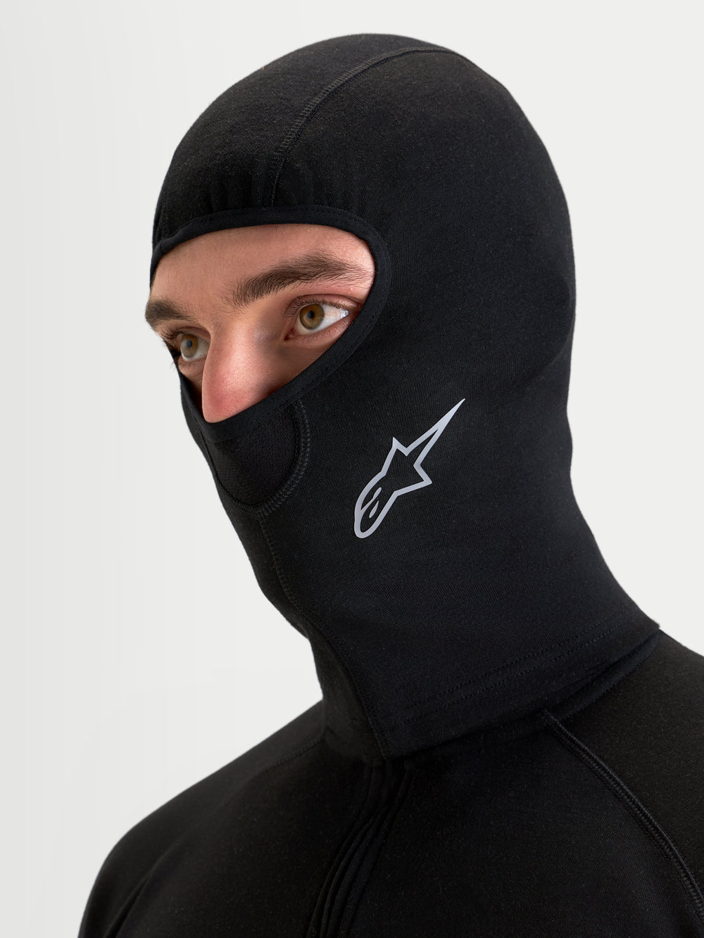 Alpinestars AT-8 Merino Balaclava, black all-terrain motorcycle balaclava worn by a model, showing dual-layer merino wool blend construction, extended neck coverage, and white Alpinestars logo branding on the side