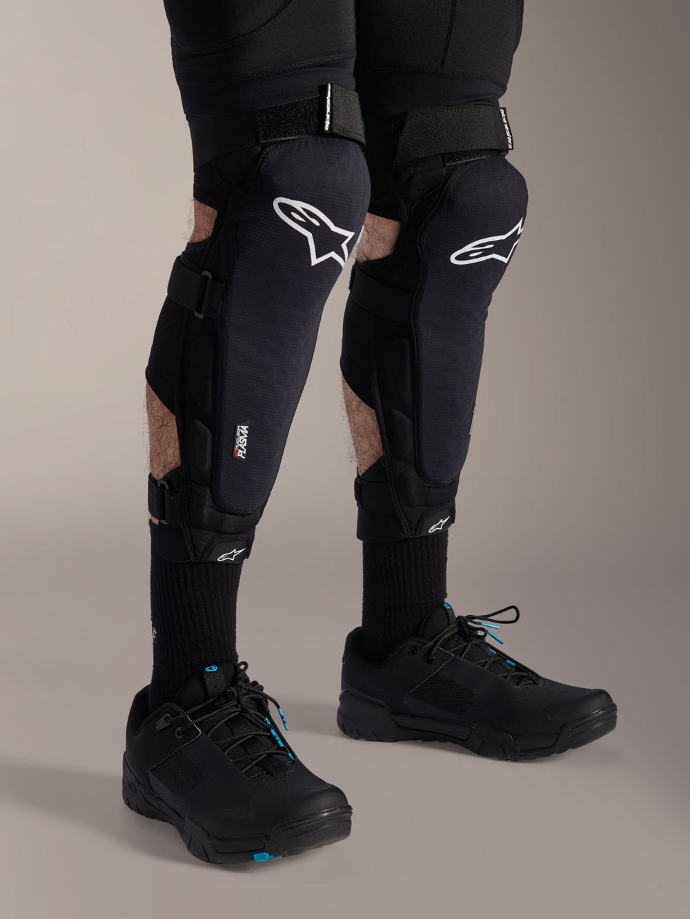 Alpinestars A-Impact Plasma Pro Knee Protectors, Black and White, featuring Nucleon PLASMA technology branding, worn with black socks and black mountain bike shoes, secure hook and loop straps, ergonomic protective gear for off-road cycling