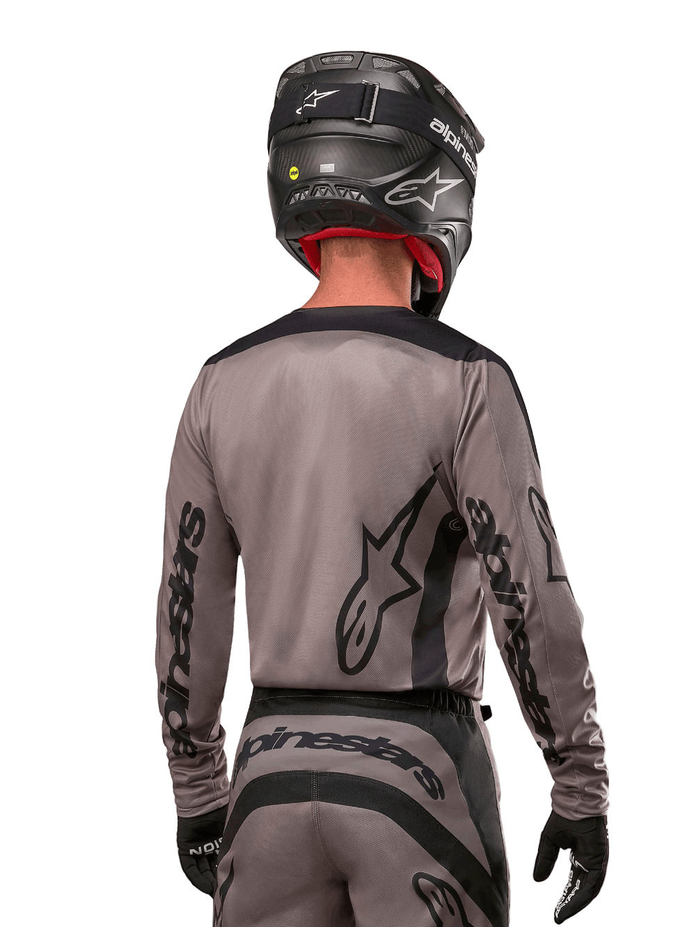 Motocross rider viewed from the back wearing the Alpinestars 2024 Fluid Lurv Jersey in Mud Black, featuring black Alpinestars branding on sleeves and back, paired with a black helmet and matching gear for off-road racing