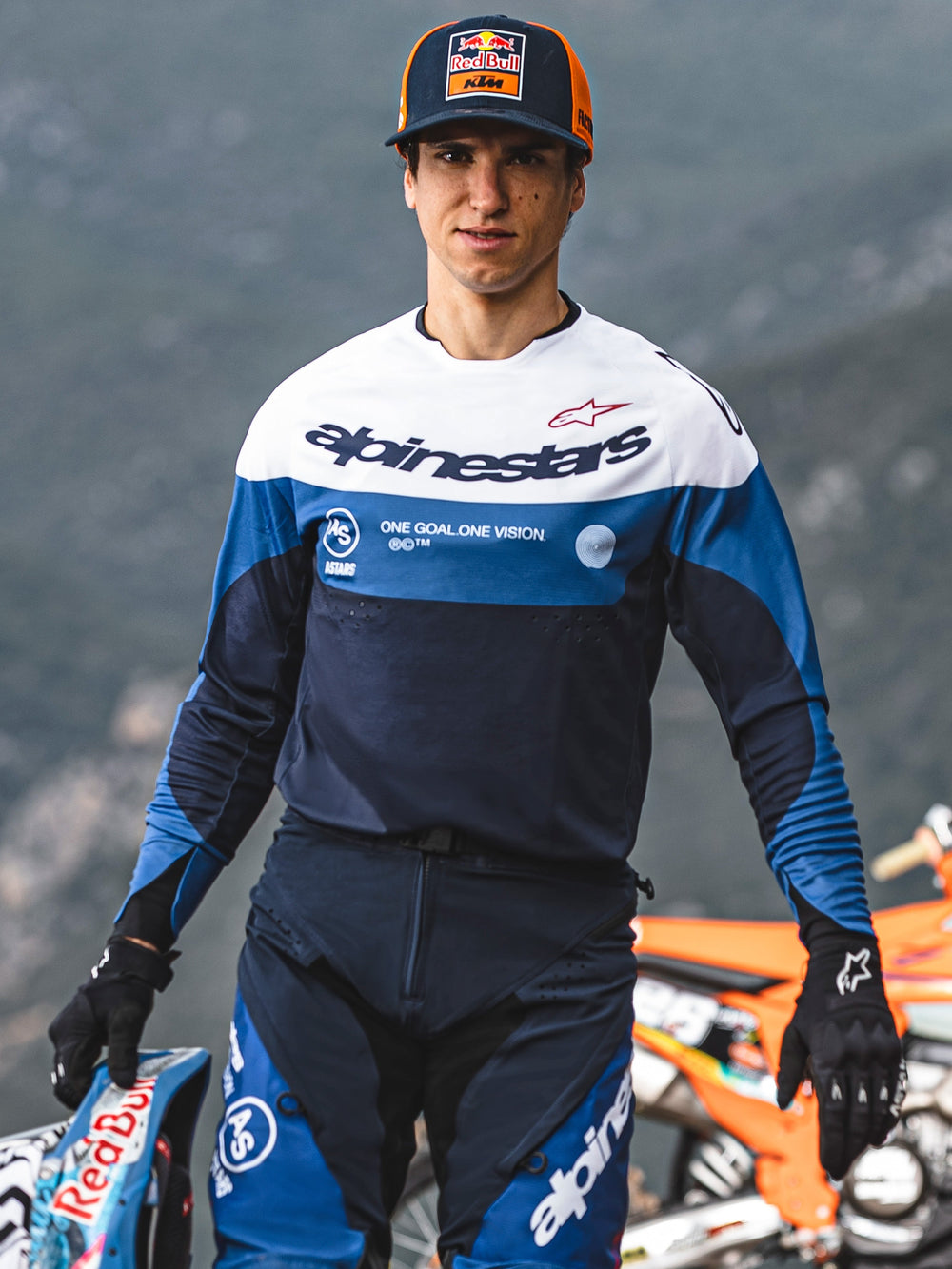 Motocross rider wearing Alpinestars Pro-Dura Jersey in Navy, Bright Blue, and White, featuring the Alpinestars wordmark and 'One Goal. One Vision.' slogan, paired with matching riding gear and a Red Bull KTM cap in an outdoor setting.