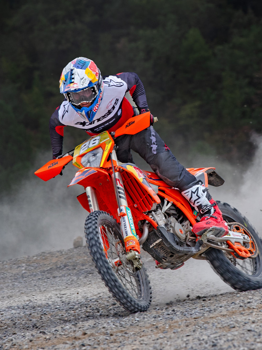Motocross rider in action wearing Alpinestars Pro-Dura Jersey in Black, Bright Red, and White, riding an orange dirt bike on a dusty off-road trail, paired with black pants and red and white boots